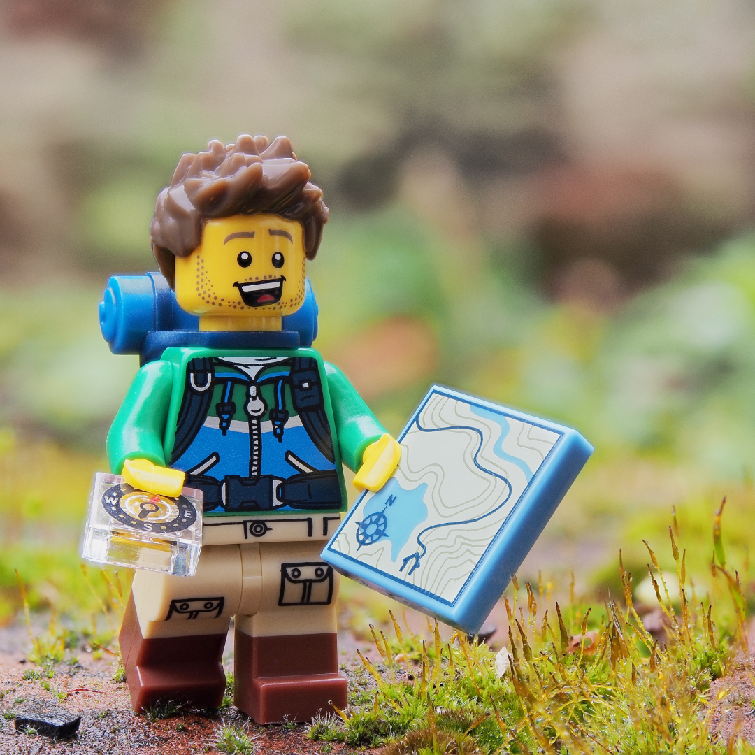 Lego man on an outdoor adventure holding a map and compass