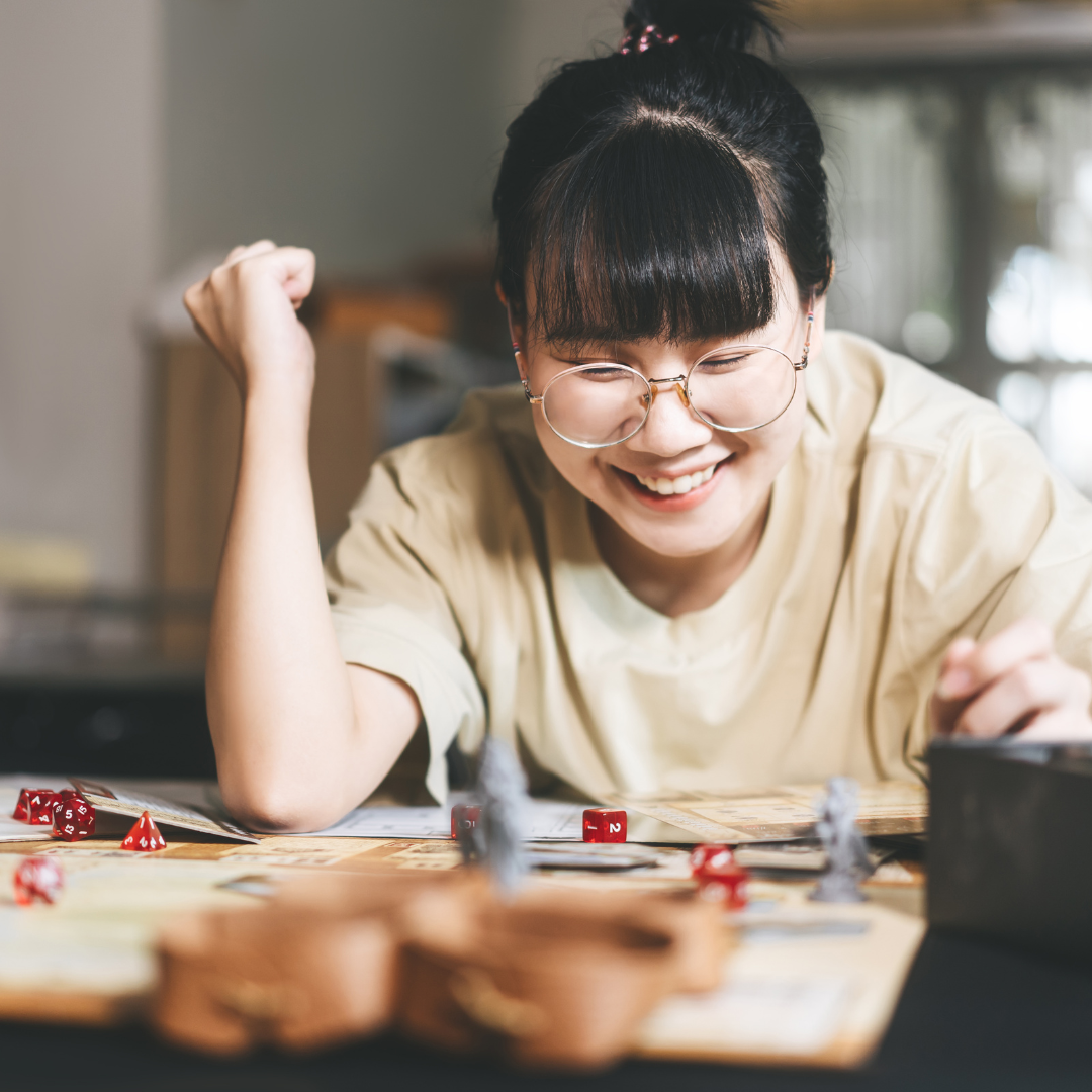 Young feminine-presenting individual playing a tabletop game and smiling.