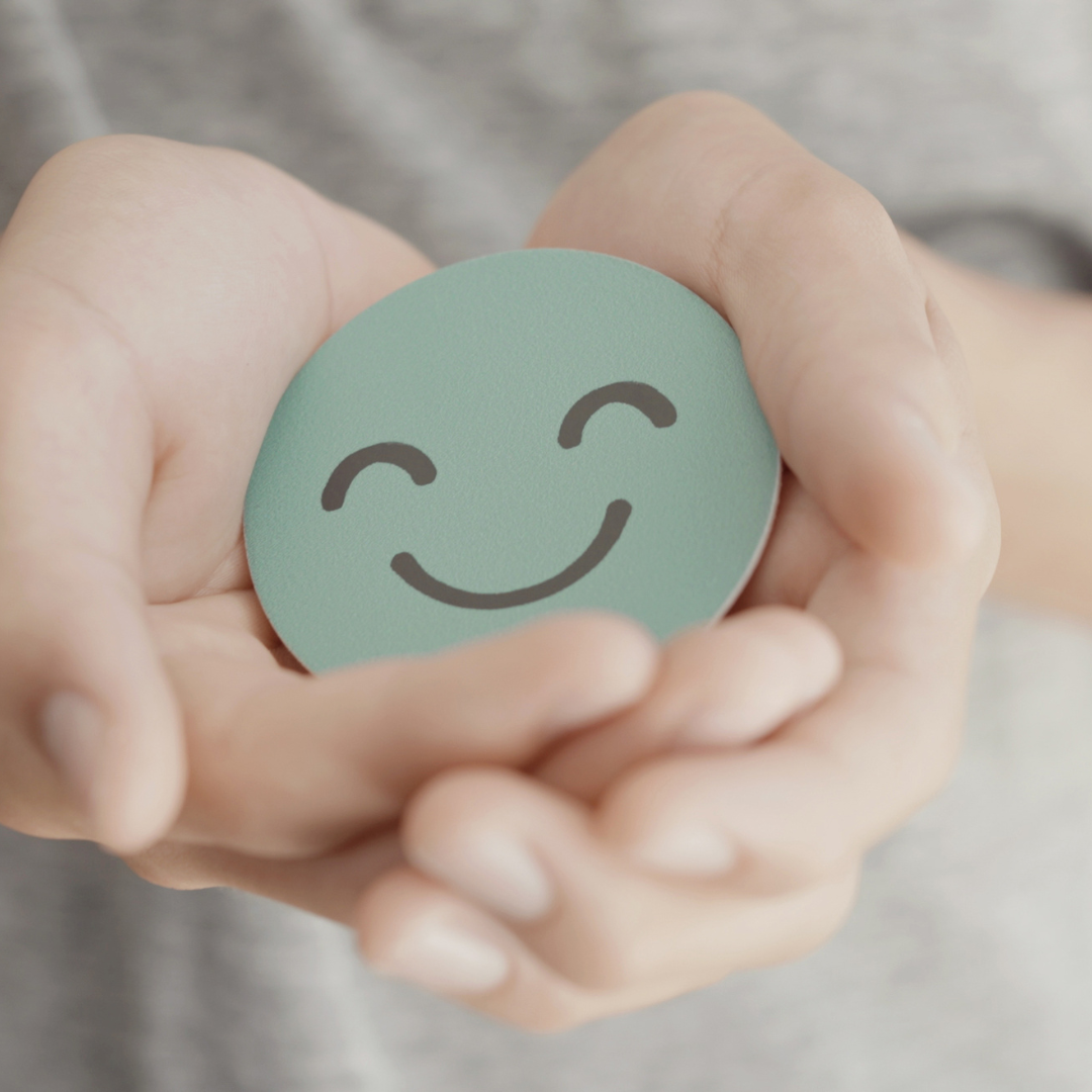 Photo of white hands holding a light green circle with a smily face