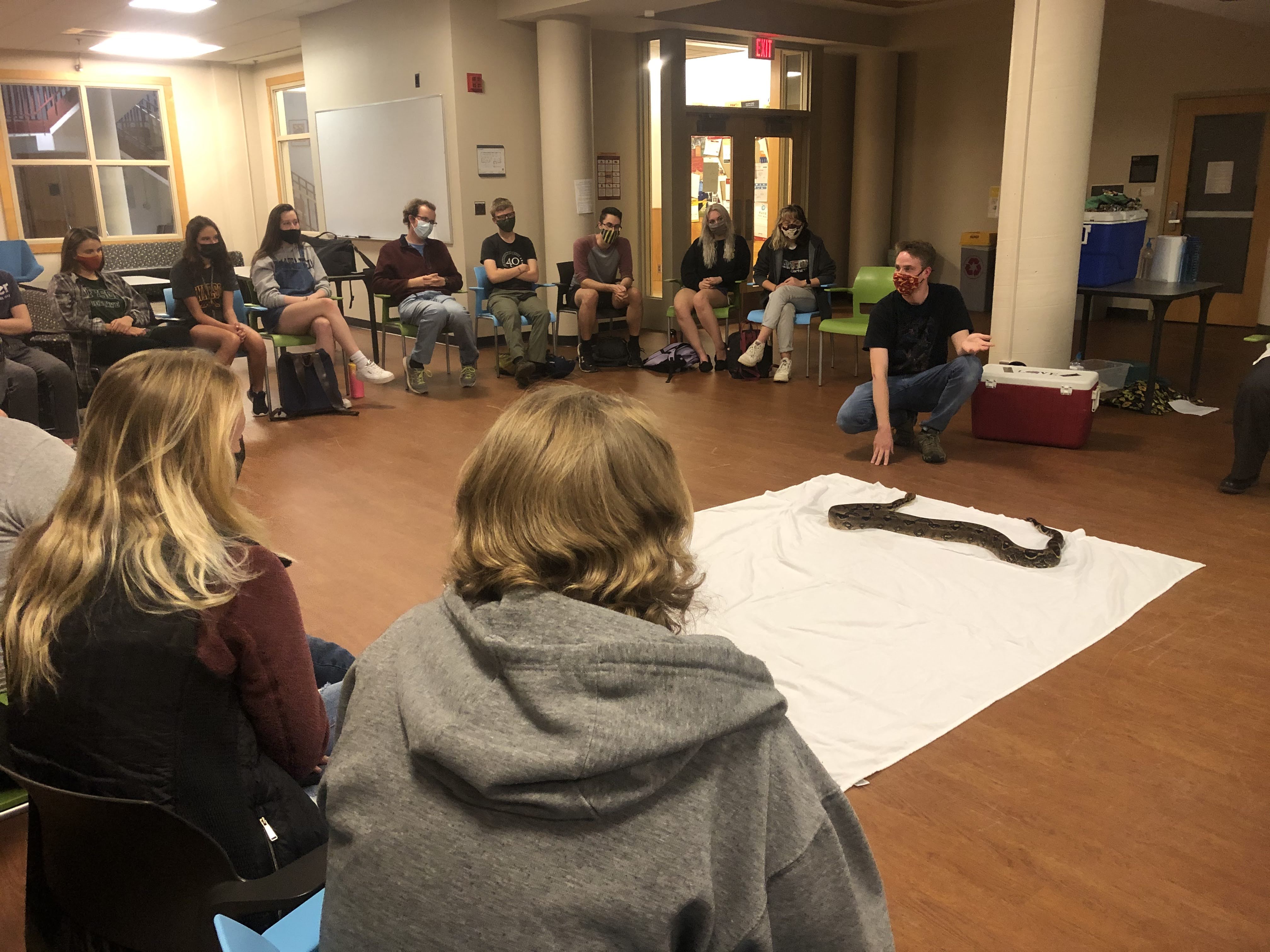 Students sitting in a circle around a boa constrictor on the floor
