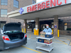 A masked hospital worker standing outside an Emergency Room exit with a large cart of food donated by local restaurants and delivered by Feed the Front Lines.