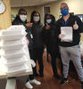 Masked employees giving the "thumbs up" sign as they stand next to a large stack of lunches delivered by Feed the Front Lines.